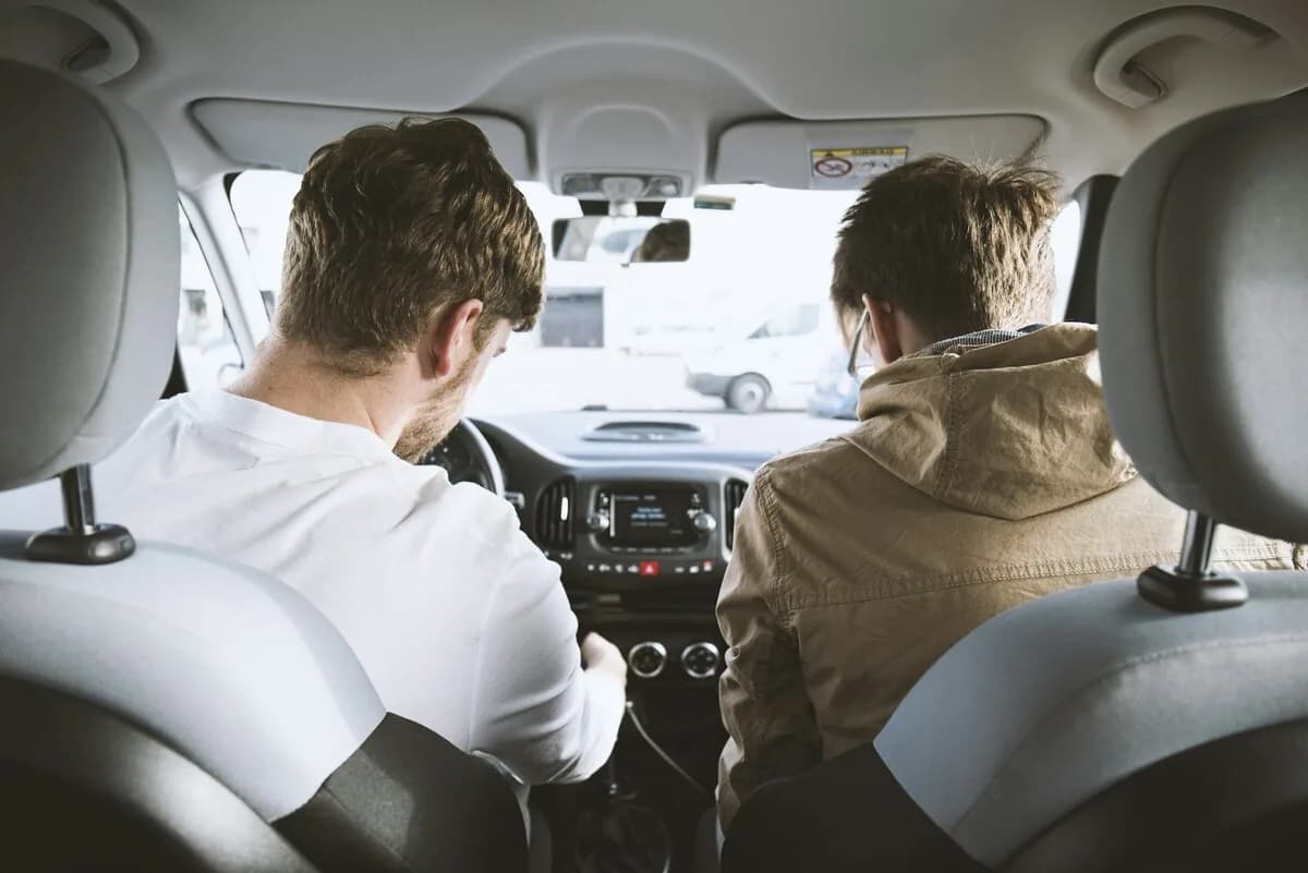 Two men inside a car during a driving lesson, instructor beside the student