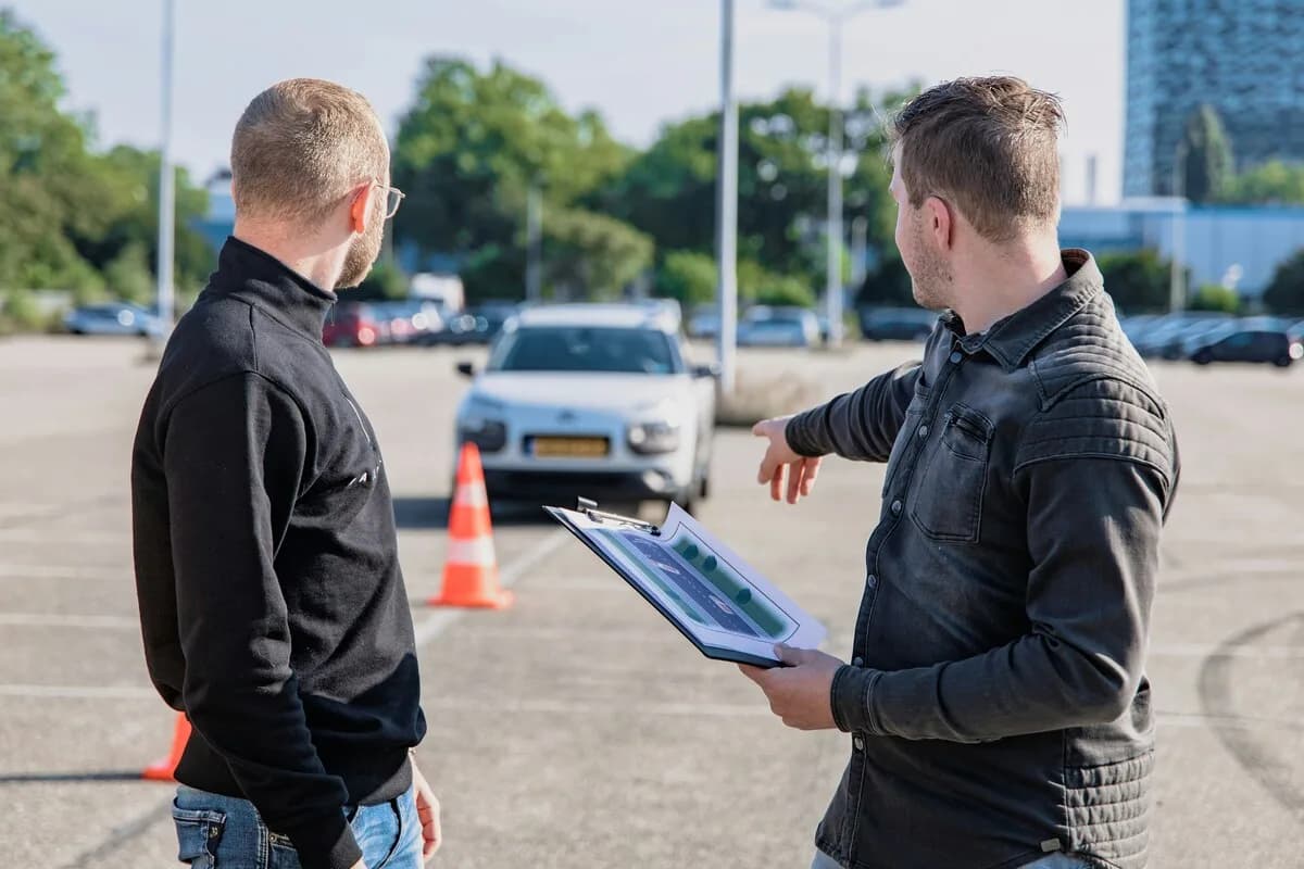 Driving instructor explaining a manoeuvre to a student in a parking lot with traffic cones
